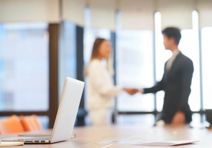 close up on laptop with blurred businesspeople hand shake together for success meeting concept