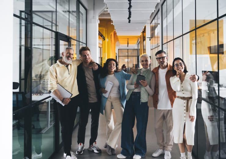 Group of diverse colleagues smiling and standing together in office corridor